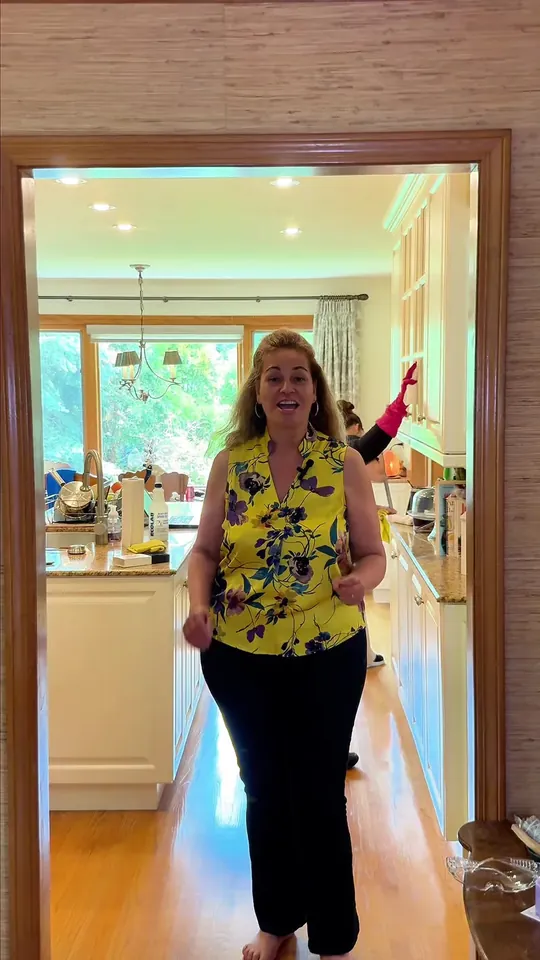 A woman in a yellow top walking through a bright kitchen