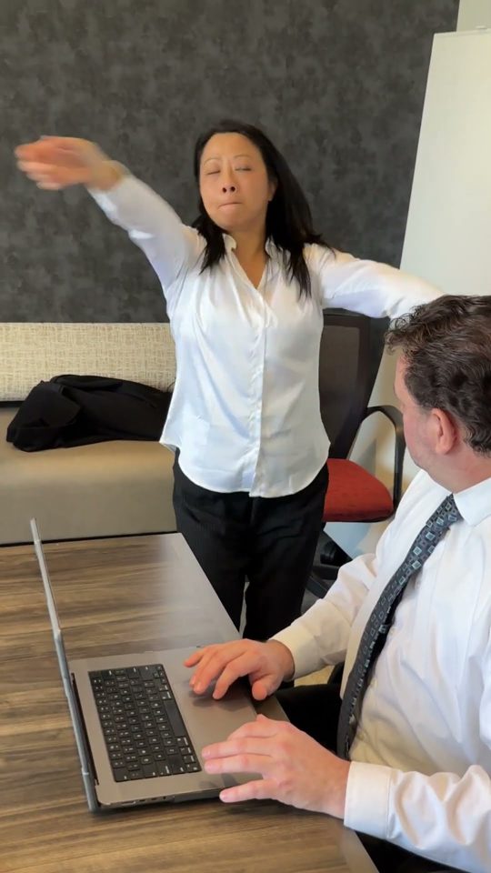 An office comedy sketch, one coworker dancing beside another at a laptop